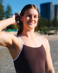 Surf life saving athlete Cyra wearing the Cacao Apsley one piece swimsuit with contrasting white shoulder straps.