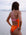 JAYD Swimwear model standing on a beach wearing the Airlie one piece cross-back swimsuit. Designed with a triple back strap for optimal support in fairy floss pink, with a contrasting orange body.