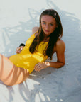 Triathlete Lauren laying on the sand at the beach in the JAYD Airlie one piece in Ignite yellow.