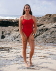 JAYD athlete Jenaya Massie standing on a beach wearing the Airlie one piece in Ruby red.