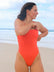 Open water swimmer Madi wearing the Albi one piece in Blaze red, standing on a beach gazing into the distance.