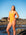JAYD athlete Mia wearing the Apsley one piece weimsuit in neon orange, standing on a beach in the afternoon surrounded by rocks and water.