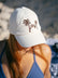 JAYD  model sitting on a beach wearing the cream JAYD Swimwear baseball cap.