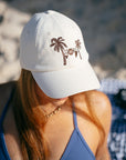 JAYD  model sitting on a beach wearing the cream JAYD Swimwear baseball cap.