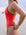 JAYD model wearing the bold Lennox one-piece swimsuit in blaze with contrasting brown cacao shoulder straps and hip panels, standing outdoors near the water with a blurred beach in the distance.