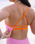 Close-up back view of the Airlie one piece triple back strap in flare orange, contrasting against the fairy floss pink swimsuit body.