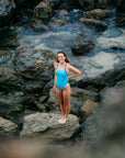 JAYD Swimwear athlete Molly standing next to a rock pool wearing the JAYD Ibiza one piece swimsuit in nautical mykonos and cobalt blue contrasting shades.