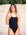 JAYD Swimwear model Hunter standing on a sandy beach wearing the Tallow one piece in black.