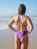 JAYD Swimwear model standing on a beach wearing the murasaki Tallow one piece swimsuit, with a secure, fixed-back design and full bum coverage fit for optimal coverage and comfort.
