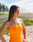 JAYD Swimwear model standing on a beach looking into the distance, wearing the Tallow one piece swimsuit in sunshine with a wide chest design for maximum support and comfort.