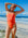 Triathlete Charlotte wearing the JAYD Zambia one piece on a beach in Blaze red with contrasting Ignite yellow shoulder straps.